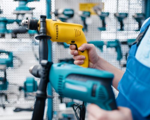 Male worker in uniform holds two electric drills in tool store. Choice of professional equipment in hardware shop, instrument supermarket
